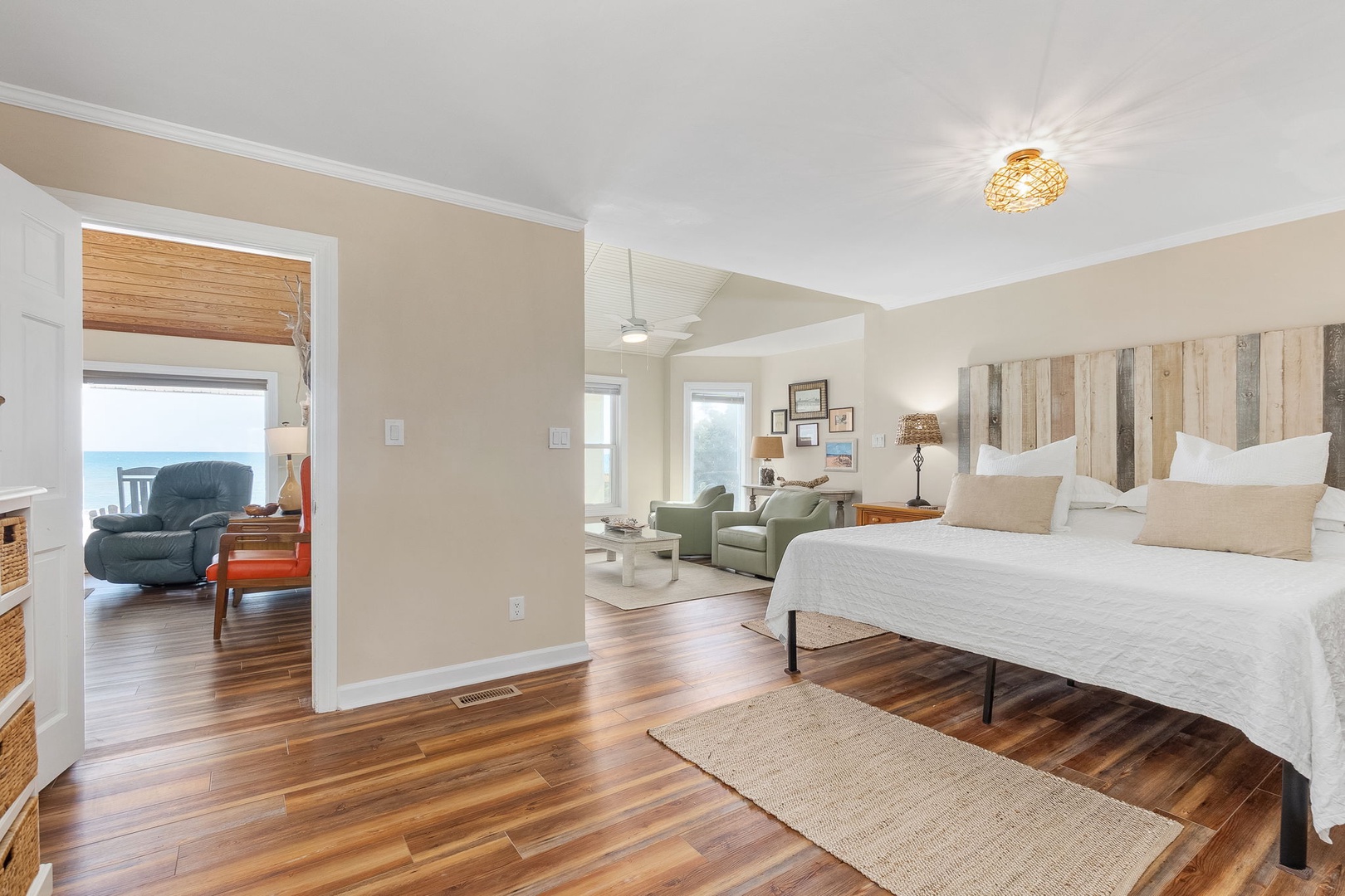 Relax in your spacious bedroom featuring gleaming hardwood floors, rustic wood headboard, and comfortable seating area with peaceful water views.