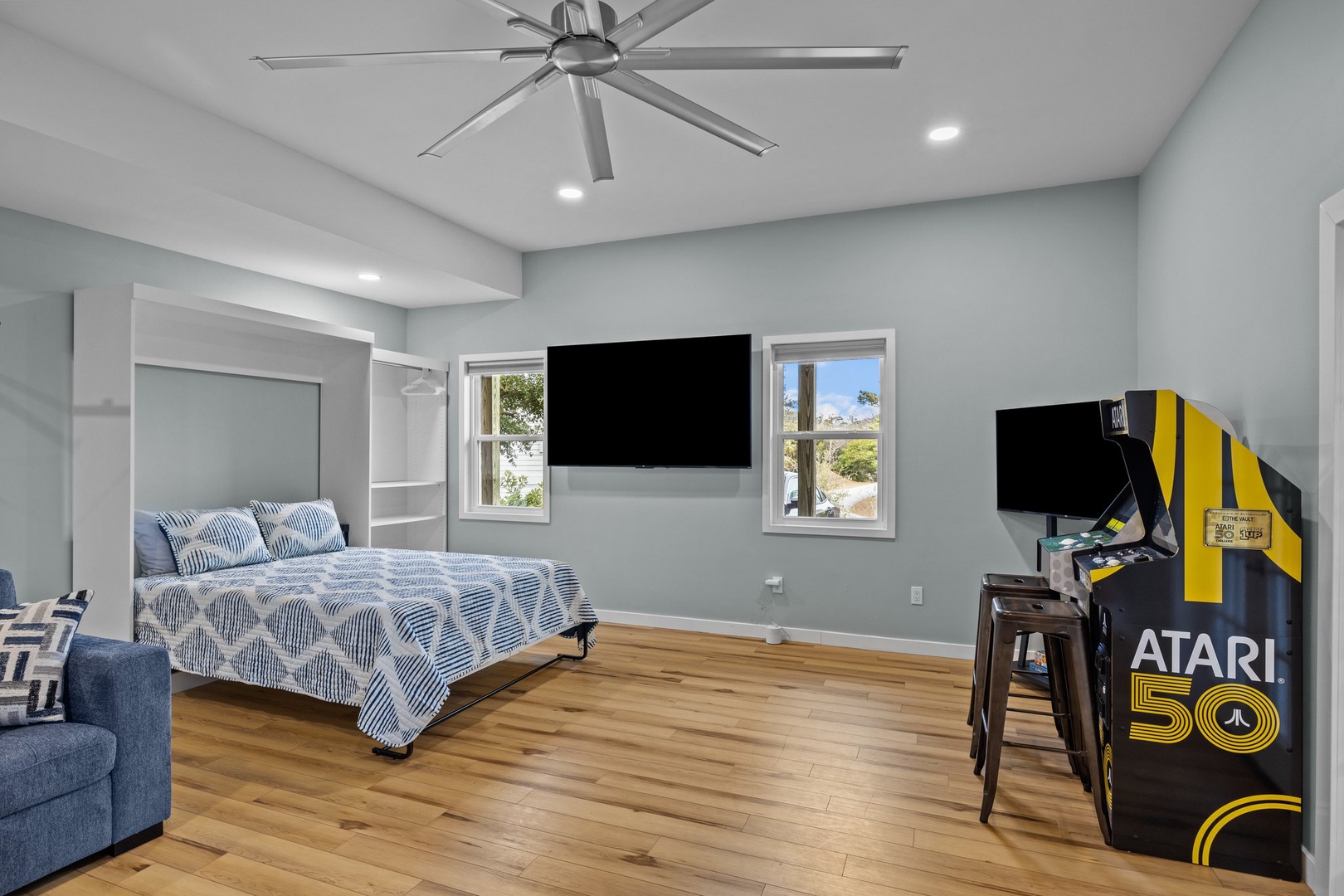 Relax in your modern bedroom featuring a cozy bed, ceiling fan, wall-mounted TV, and classic arcade gaming for endless entertainment.
