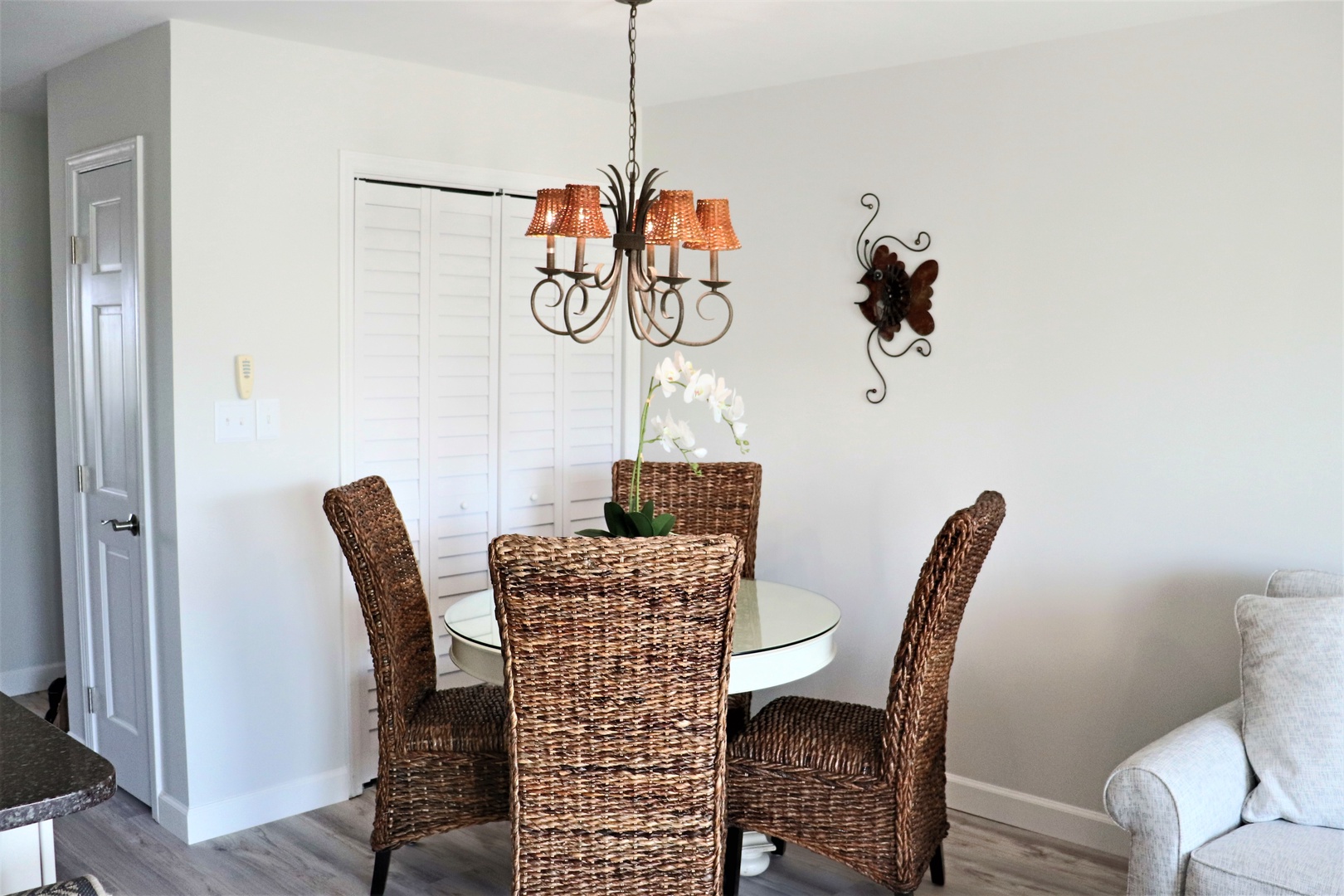 Gather around your elegant glass dining table with wicker chairs under warm chandelier lighting for memorable meals together.