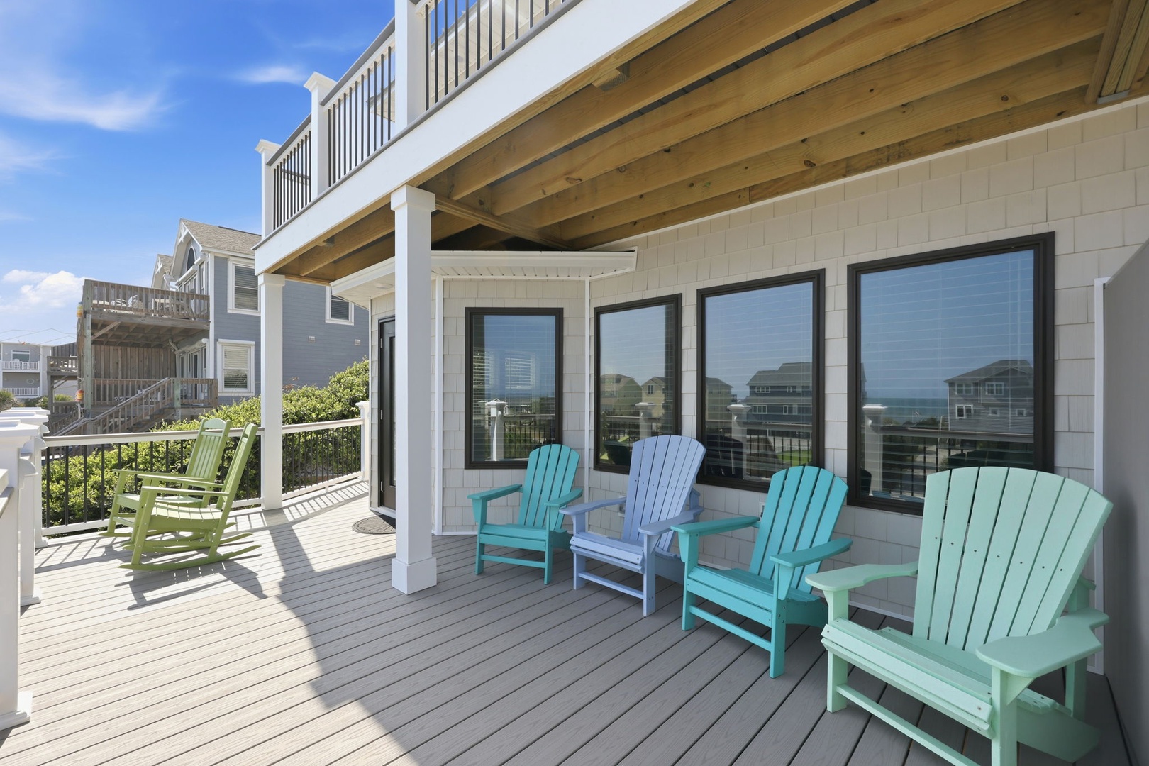 Coastal-style deck features Adirondack chairs in ocean hues, offering a peaceful spot to unwind with views of the surrounding beach community and glimpses of the water beyond.