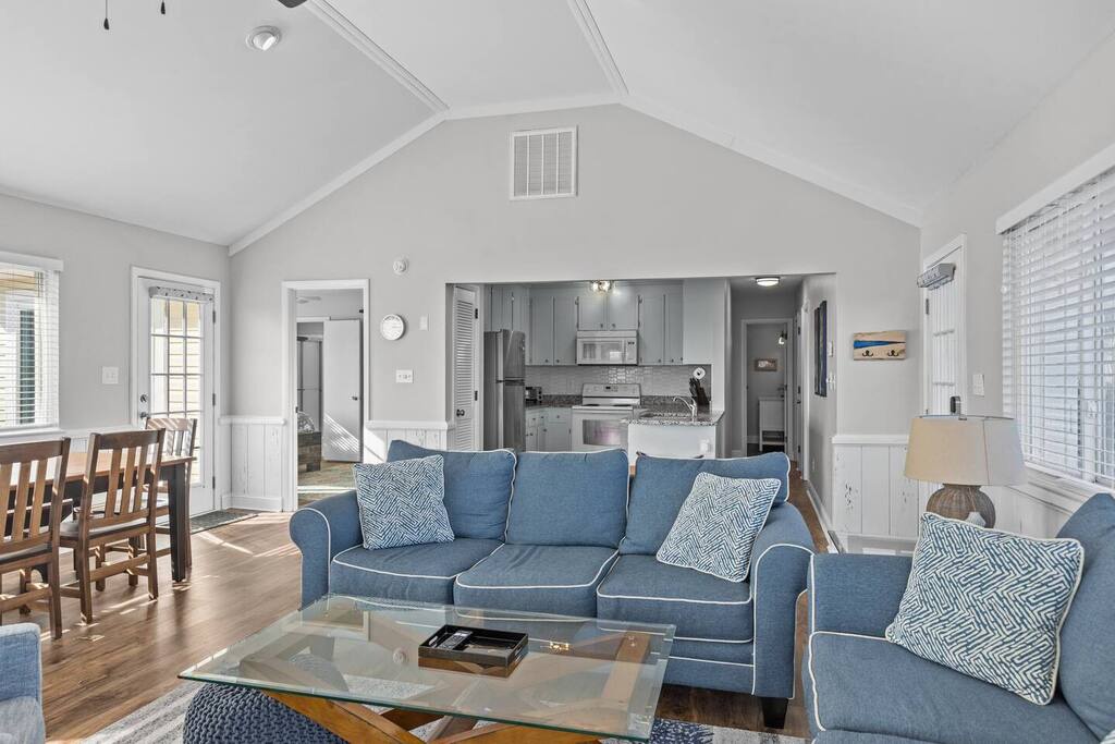 Relax in your spacious open-concept living area with vaulted ceilings, comfortable blue seating, and a fully equipped kitchen.