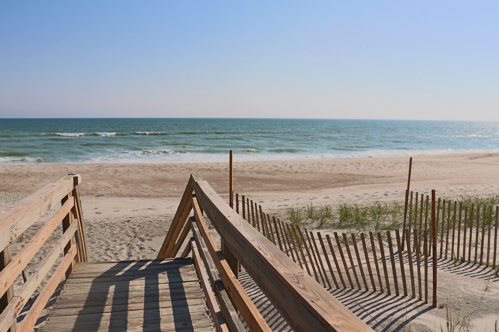 Pristine beach access with wooden boardwalk leading to soft sand and gentle waves under endless blue skies.