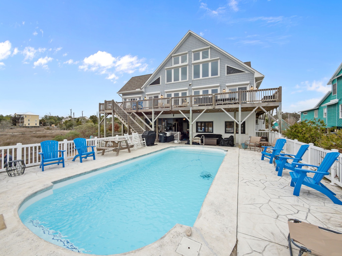 Coastal beach house featuring private pool, spacious deck, and vibrant blue chairs for perfect waterfront relaxation.