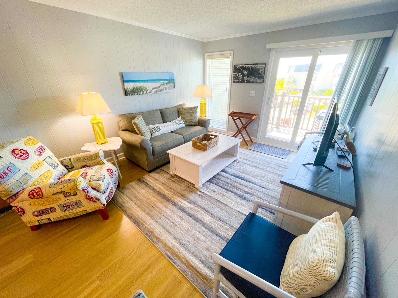 Unwind in your bright coastal living room with plush seating, beach artwork, and private balcony access.