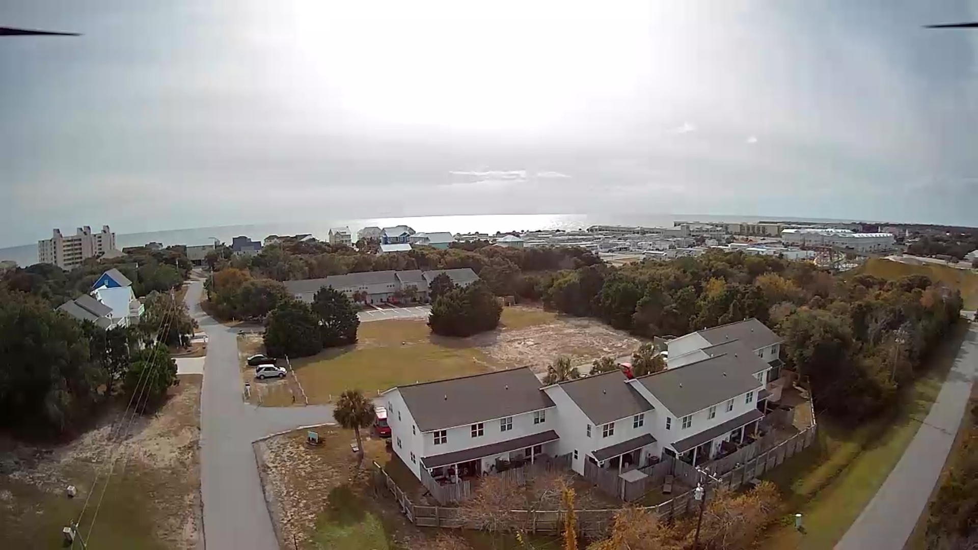 Aerial view of coastal property featuring modern multi-unit building with decks, nestled between trees and residential neighborhood near the beach.