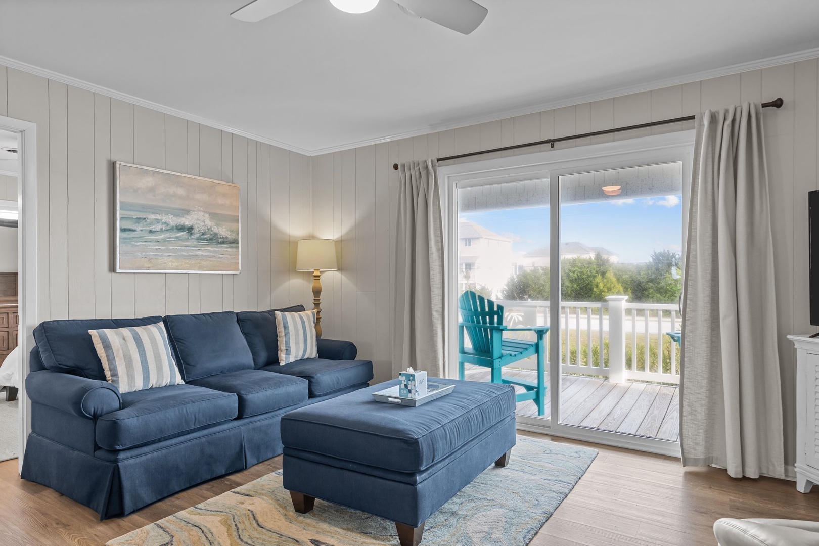 Relax in your coastal-inspired living room featuring plush navy seating, natural light, and private deck access for the perfect beach getaway retreat.