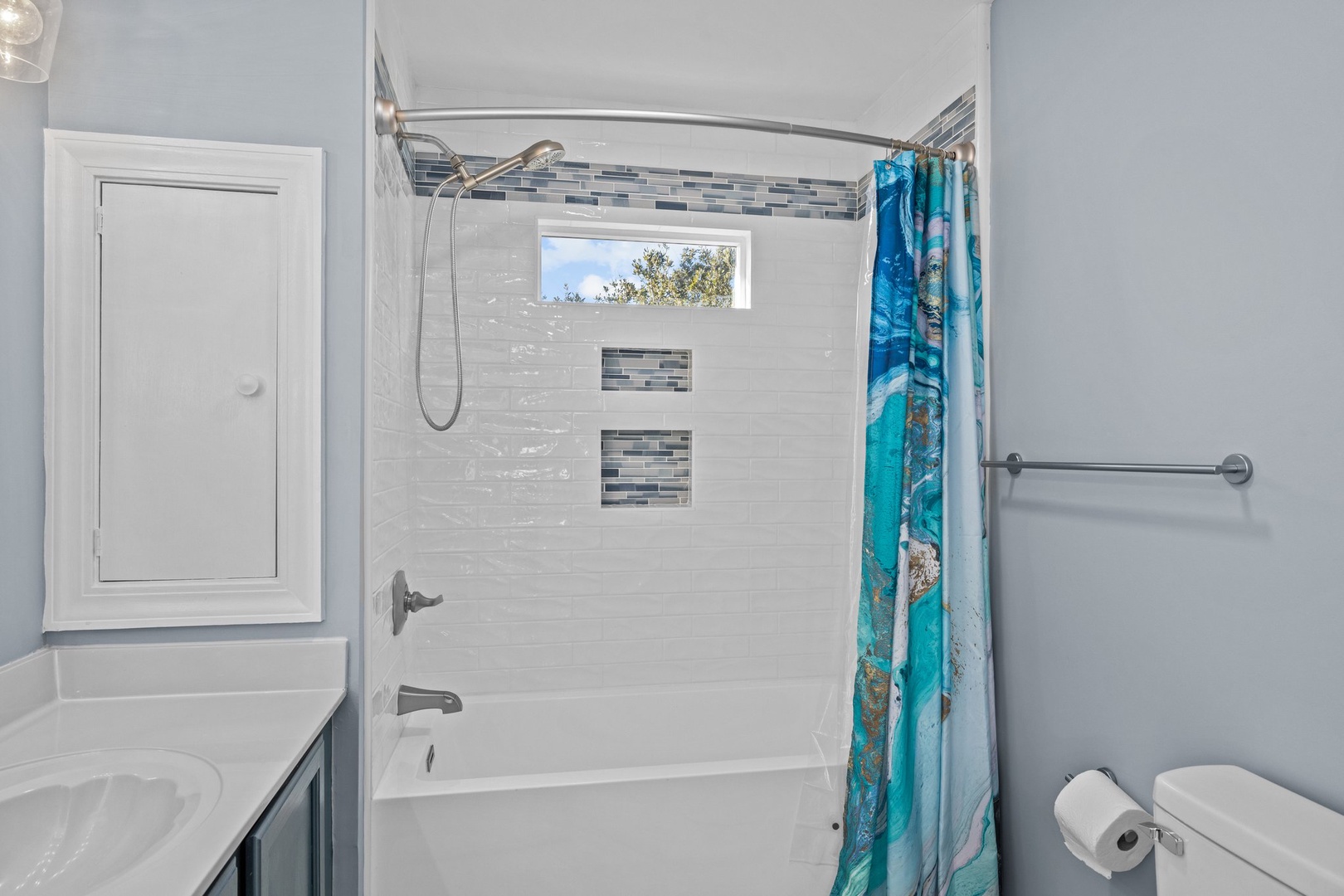 Relax in your modern bathroom featuring a tub-shower combo with decorative tile accents and ocean-themed touches.