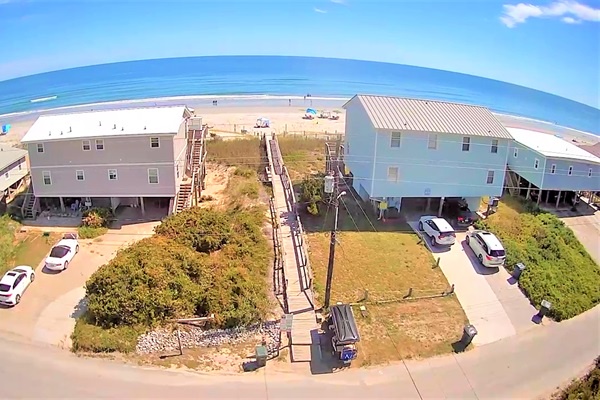 Beachfront property complex with wooden walkway leading directly to pristine sandy shores and sparkling ocean waters.