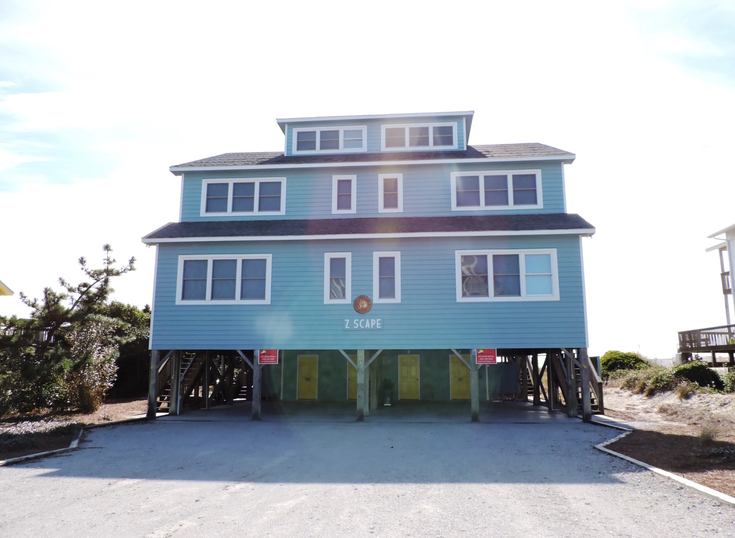 Charming three-story beach house elevated on stilts with bright turquoise siding and multiple windows for ocean breezes.