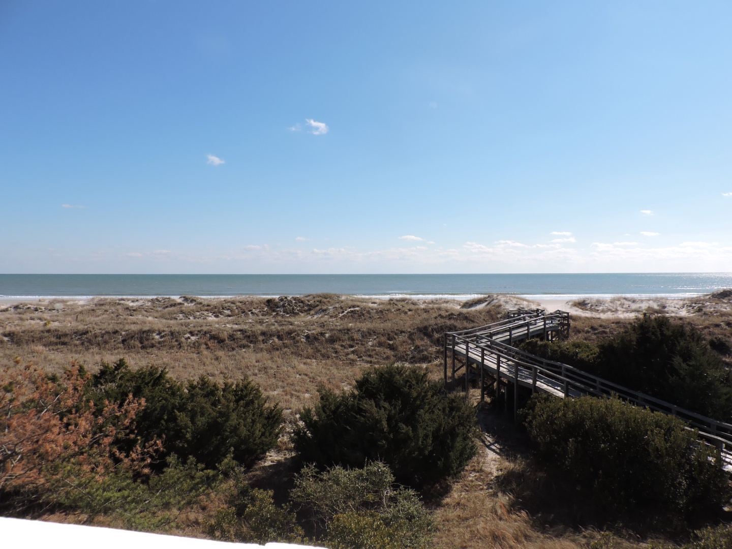 A wooden boardwalk leads through coastal dunes to pristine sandy shores under endless blue skies.