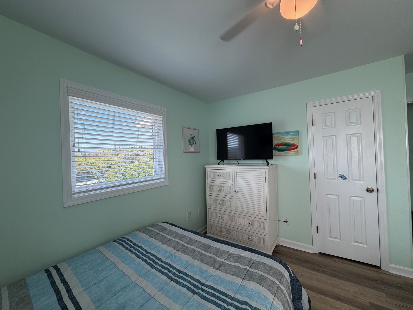 Relax in this tranquil mint-green bedroom where coastal breezes flow through white blinds and your TV awaits.