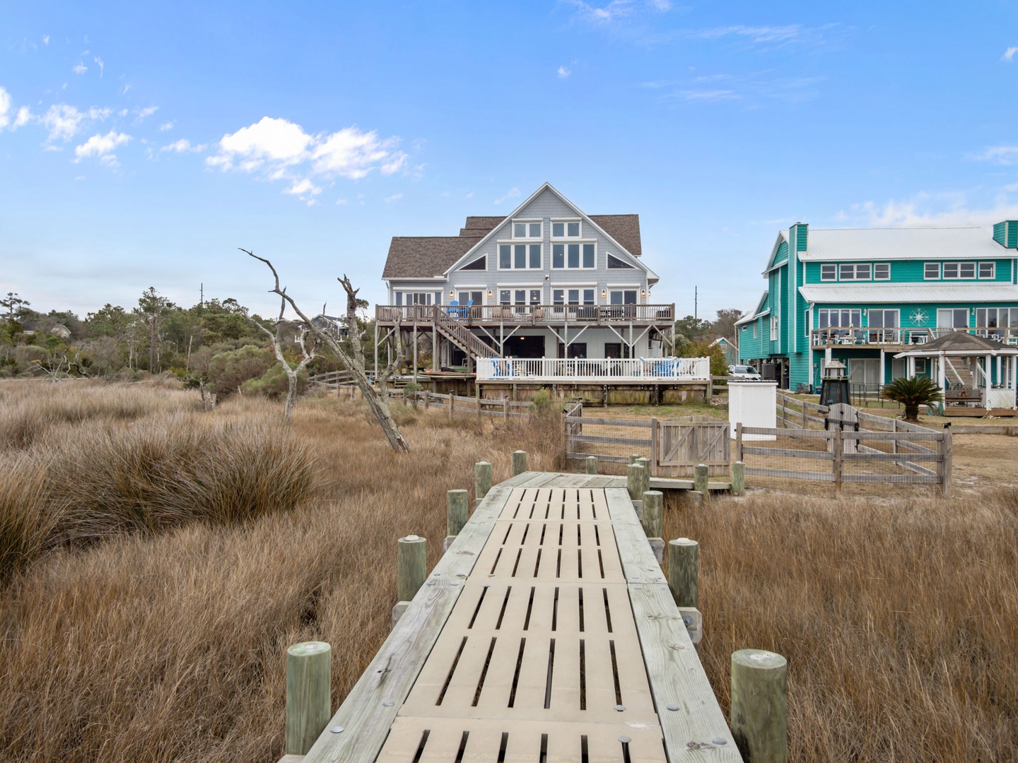 Elevated beach houses overlooking protected salt marshlands, connected by wooden boardwalks through the coastal dunes.