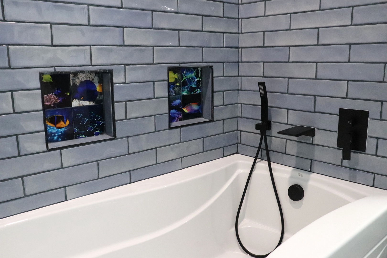 Sink into this sleek soaking tub framed by white subway tiles and playful ocean-themed niches. Modern matte-black fixtures add style to your private escape.