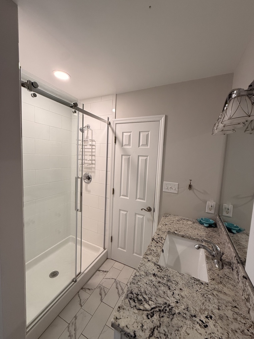 Step into your pristine bathroom featuring a spacious walk-in shower with elegant glass doors, gleaming granite countertops, and crisp white subway tile for your comfort.