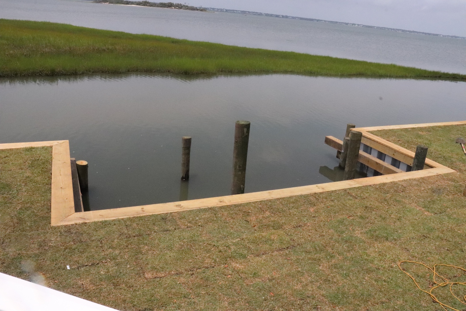 Waterfront dock construction in progress overlooking tranquil marshlands and distant water views.