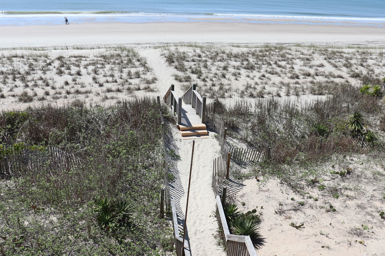 Pristine beach access via wooden walkway through protected dunes, leading to expansive sandy shores and rolling ocean waves.