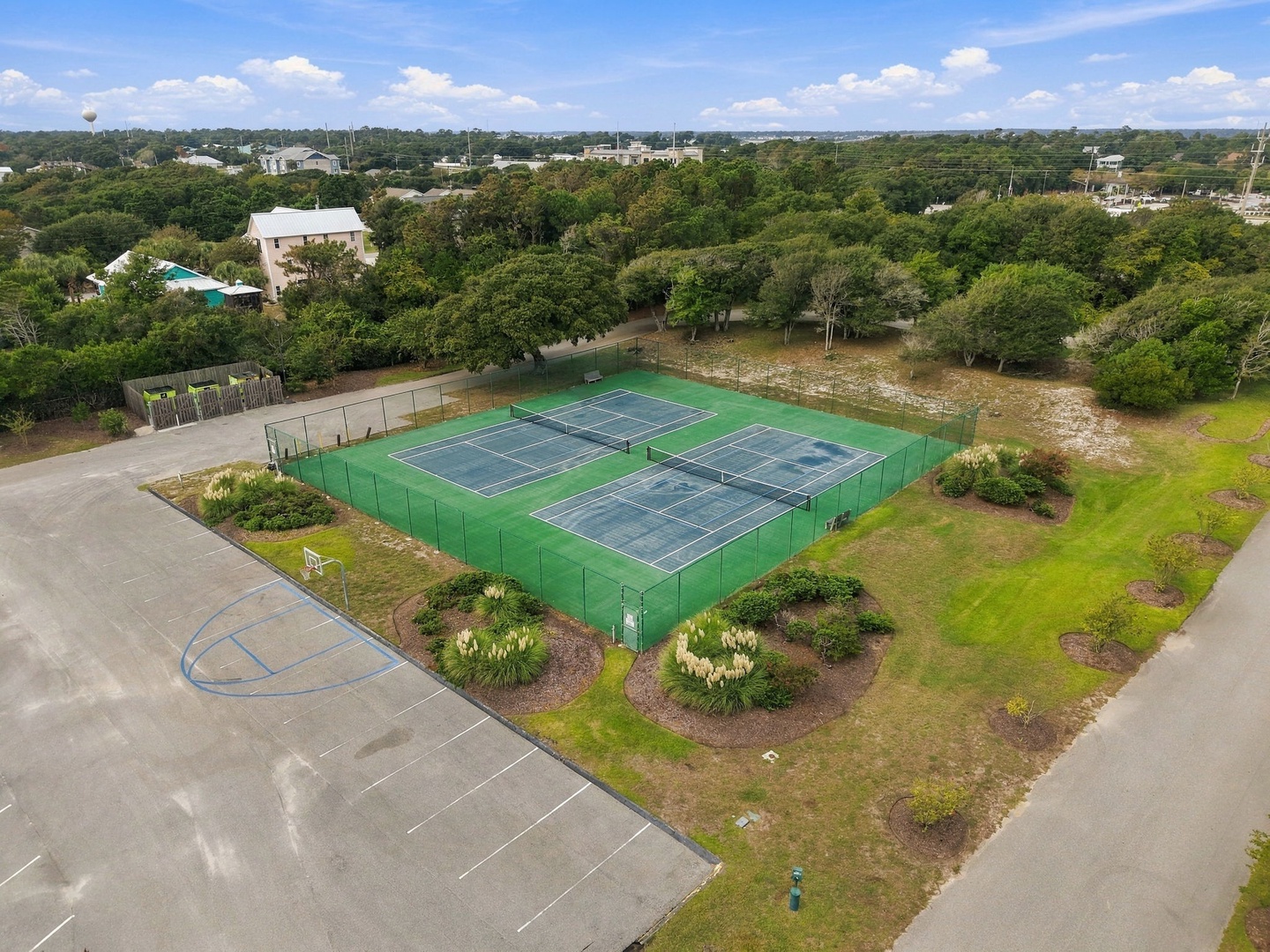 Aerial view showing the property's tennis courts nestled among lush greenery, with landscaped gardens, a basketball court, and abundant natural surroundings.