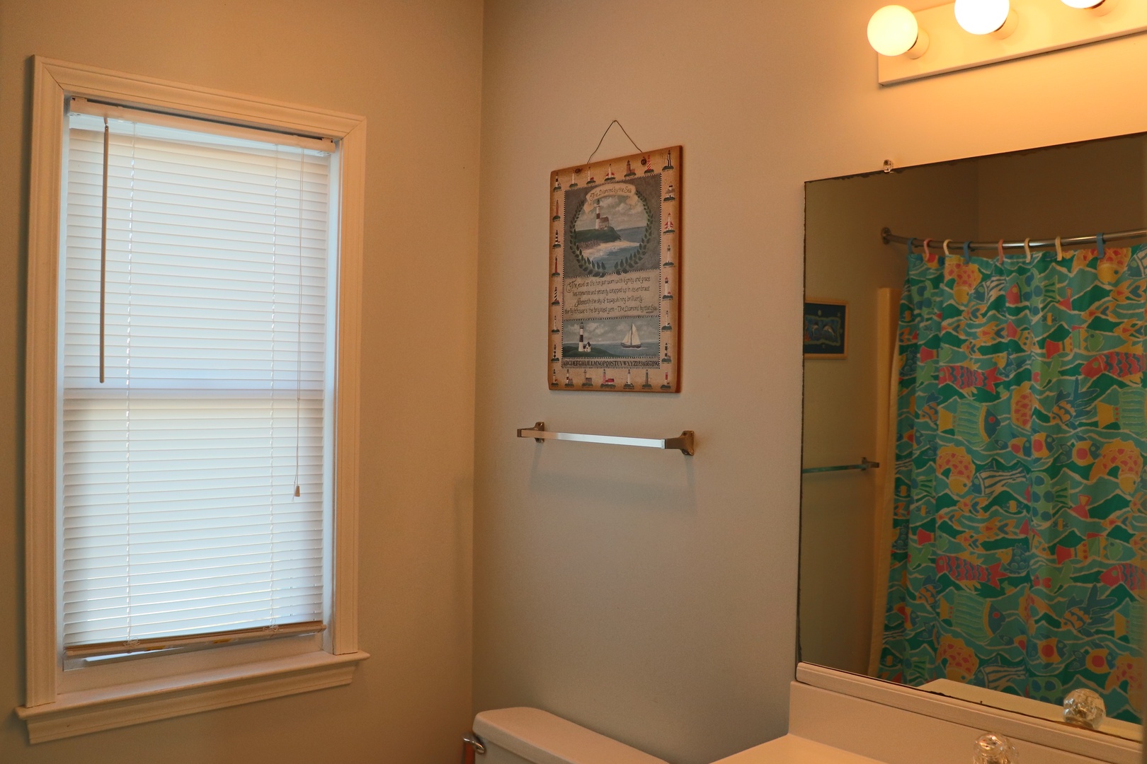 Your private bathroom features warm lighting and thoughtful touches, including a colorful shower curtain and coastal artwork that creates a welcoming retreat.