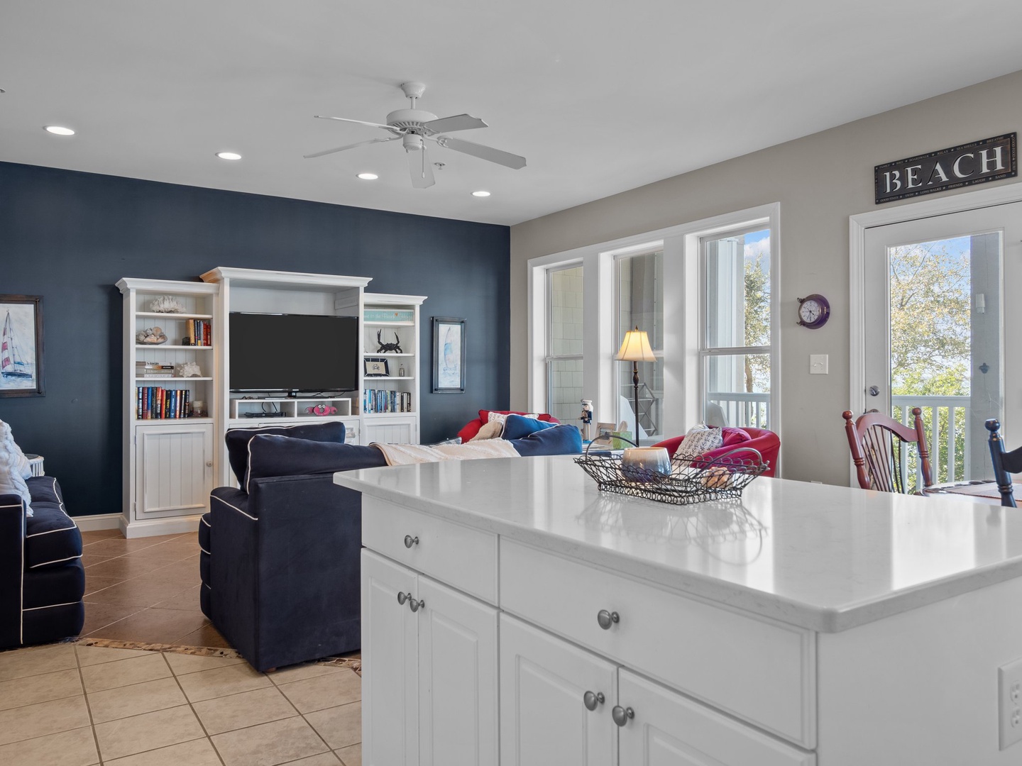 Relax in your bright coastal living space with entertainment center, comfortable seating, and natural light streaming through large windows.