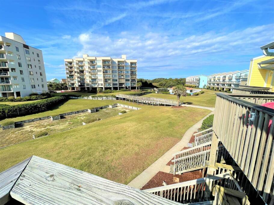 Elevated view of surrounding neighborhood with open green spaces and nearby apartment buildings under a beautiful blue sky.