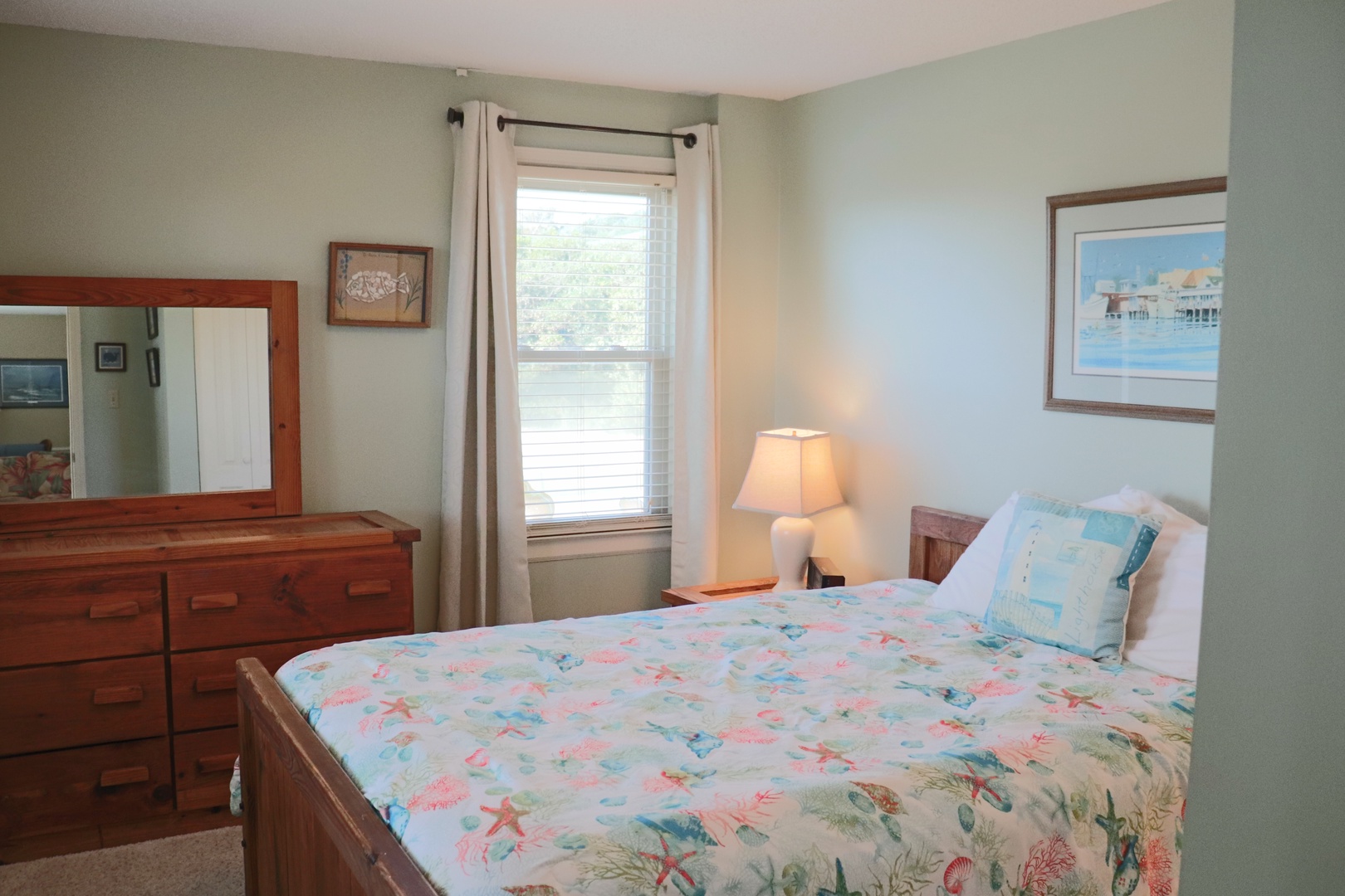 Your coastal-themed bedroom features a comfortable queen bed, warm lamplight, and peaceful water views through your private window.