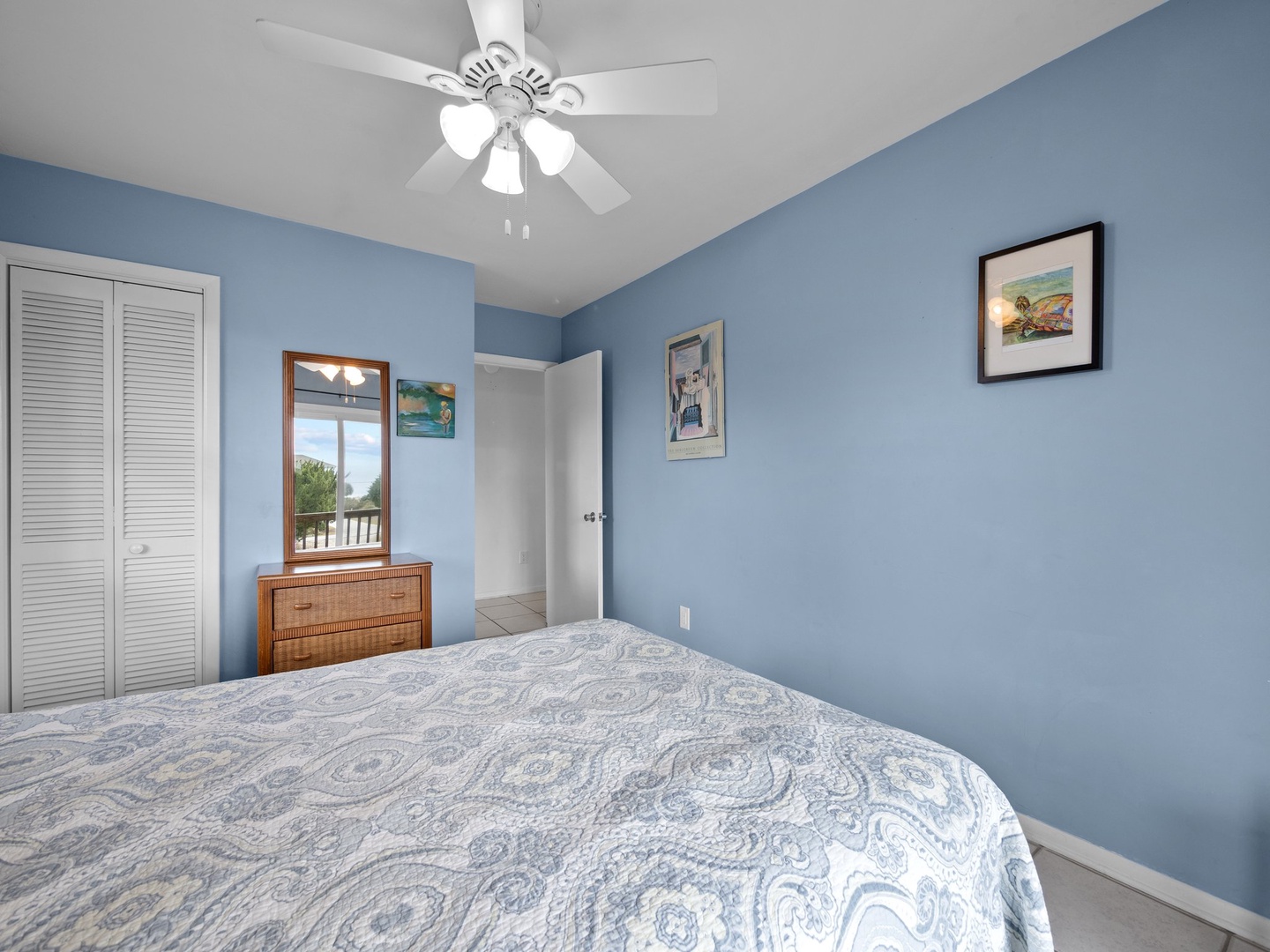 Drift off to sleep in this calming blue bedroom, where coastal artwork and gentle ceiling fan create your perfect retreat.