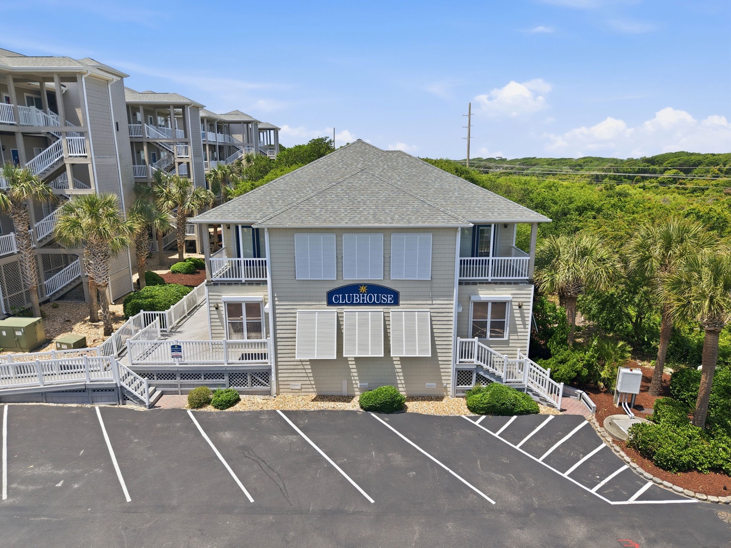 Aerial view of the clubhouse surrounded by lush coastal greenery and neighboring vacation properties, with ample parking for guests.