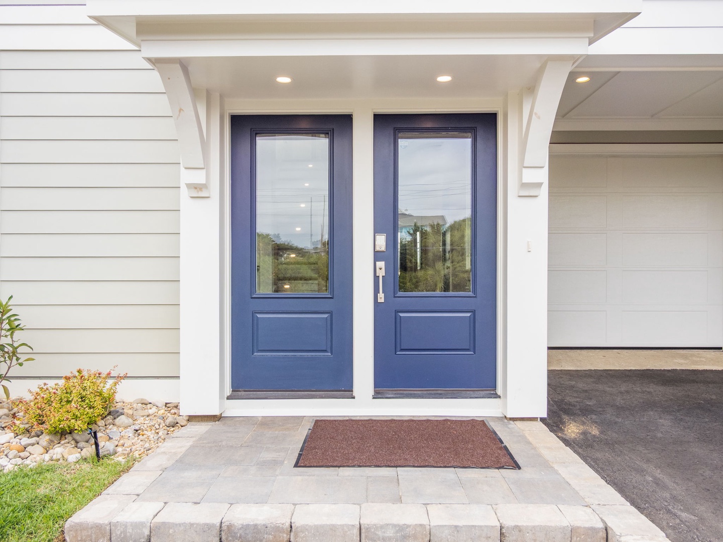 Modern home entrance with elegant blue double doors and covered porch welcomes visitors to this stylish property.