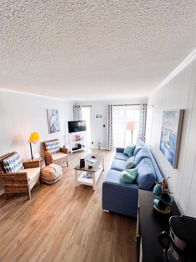 Settle into your bright coastal living room with plush blue sofa, wicker chairs, and warm wood floors for relaxing days.