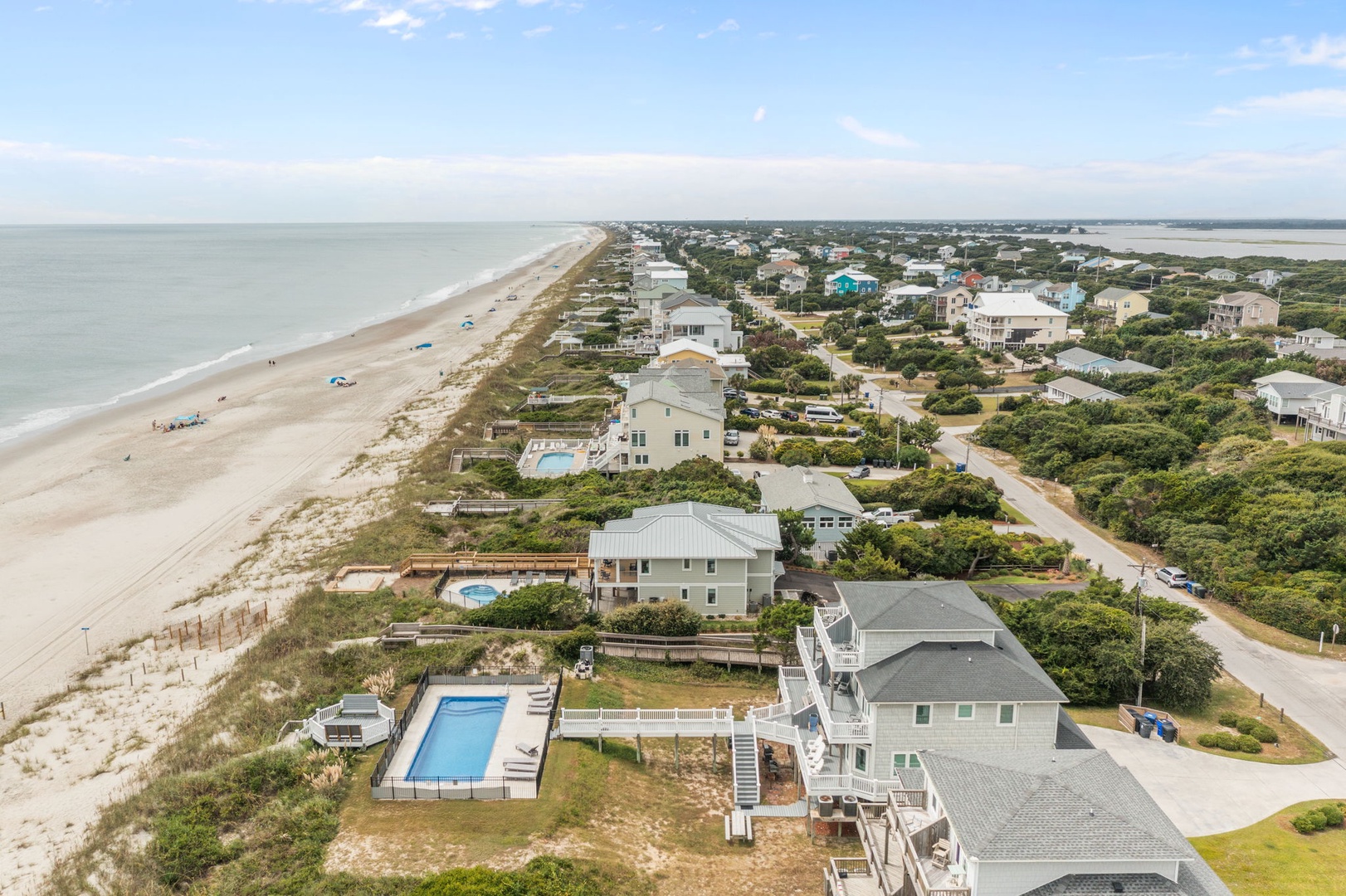 Aerial view of beachfront vacation homes with swimming pools nestled between pristine coastline and residential community.