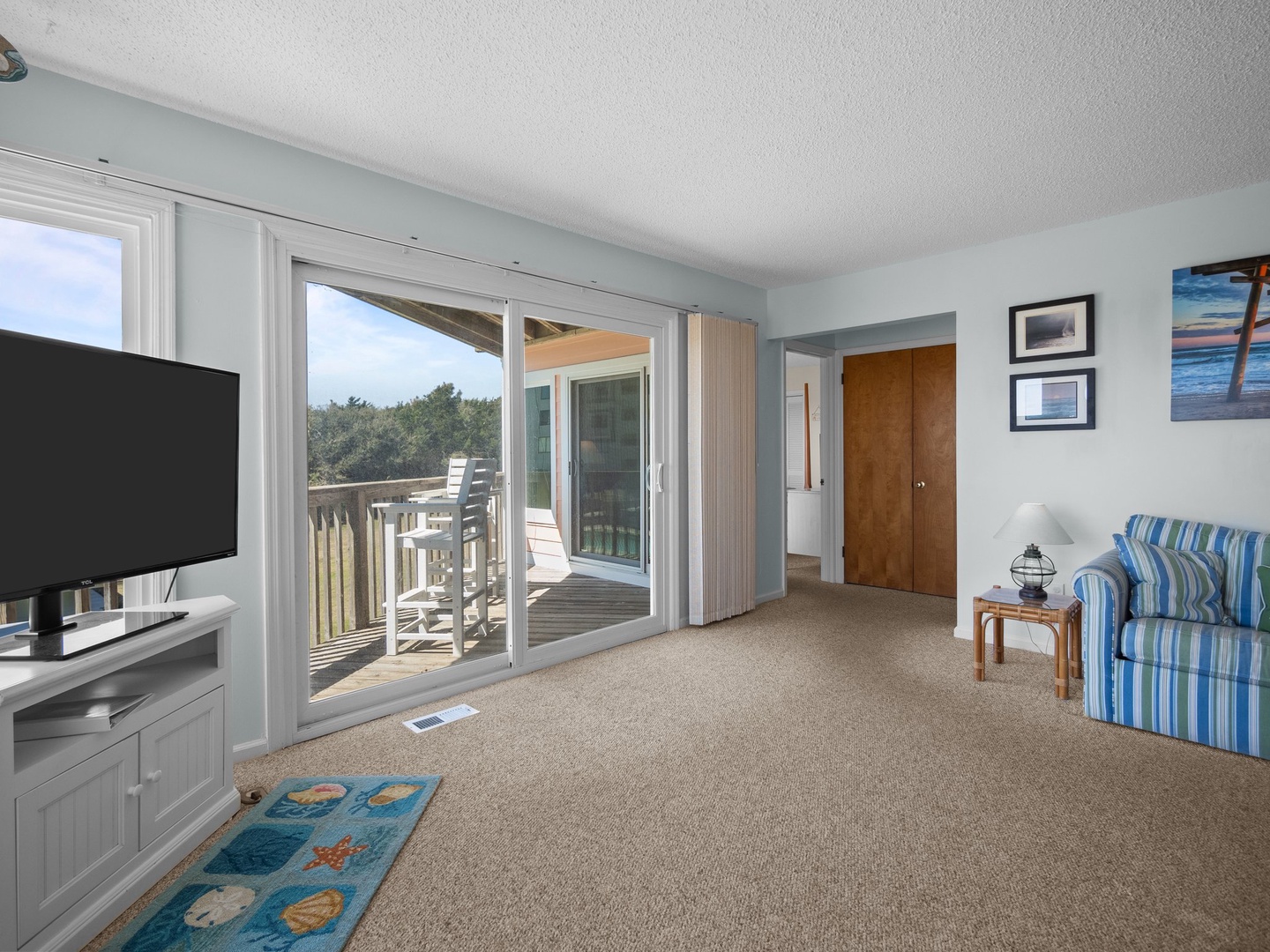 Relax in your bright living space with ocean-themed decor, flat-screen TV, and private balcony access overlooking peaceful treetops.