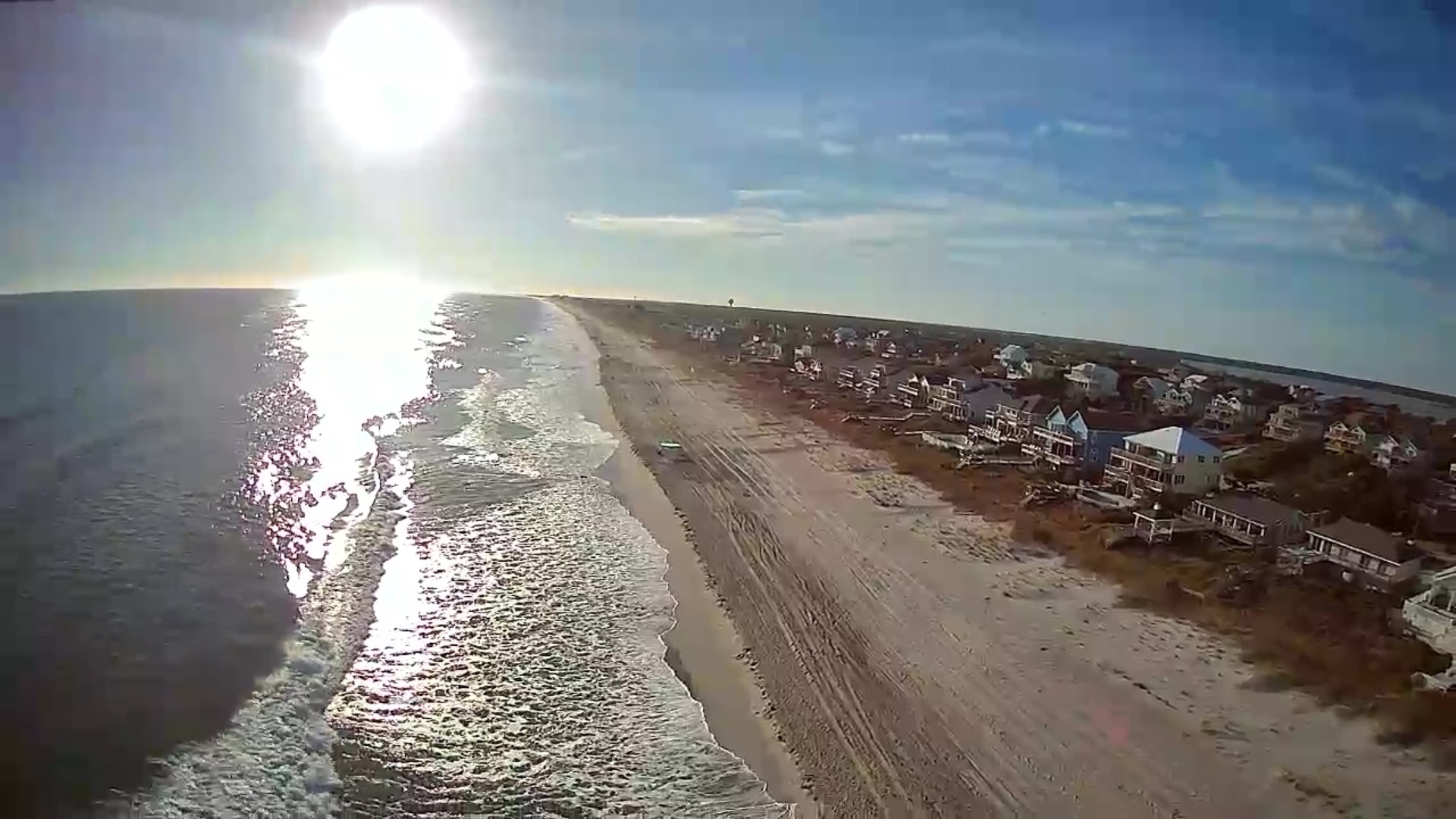 Stunning aerial view of a pristine coastal community with sparkling ocean waves meeting sandy shores and charming beach houses.