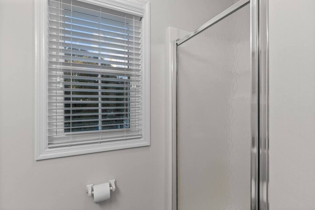Your private bathroom features a pristine glass shower with sleek fixtures and fresh natural light streaming through crisp white blinds.