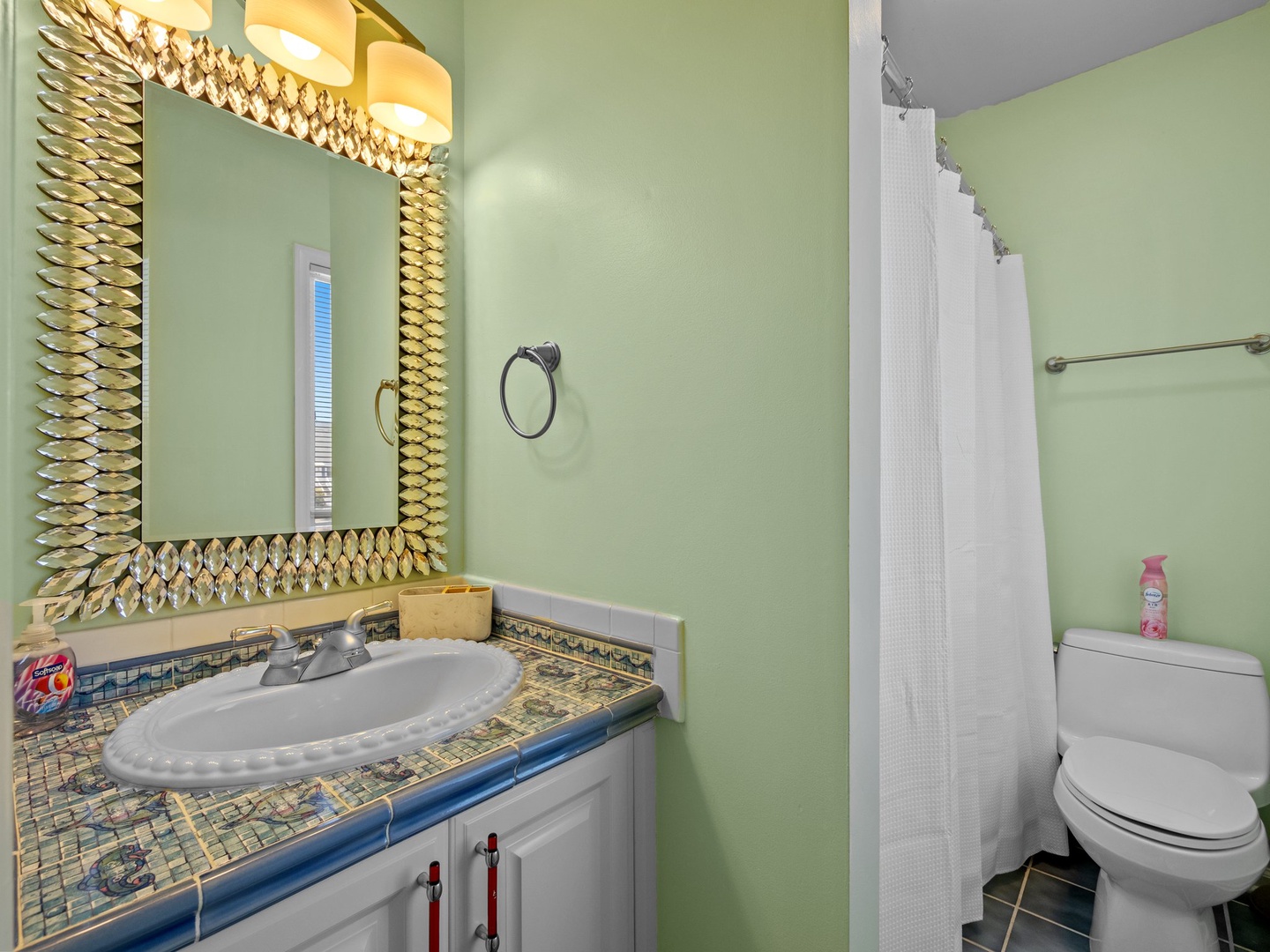 Refresh in your beautifully appointed bathroom featuring mint green walls, stunning mosaic tilework, and an elegant gold-framed mirror.