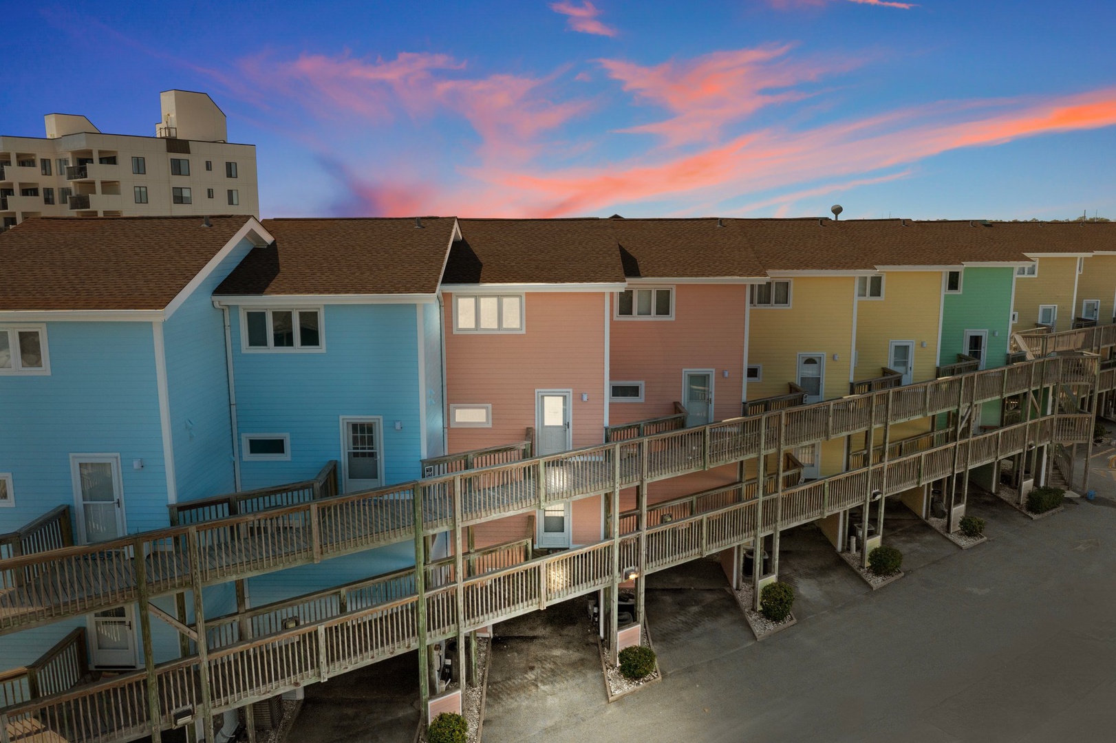 Colorful beachfront rental units beneath a stunning sunset sky, with elevated walkways connecting each coastal home.
