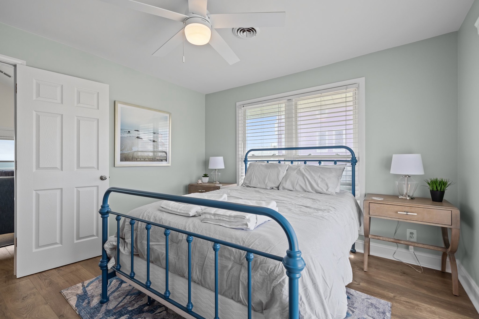 Rest peacefully in your coastal bedroom, where soft sea-green walls and a charming blue iron bed frame create your perfect coastal retreat.