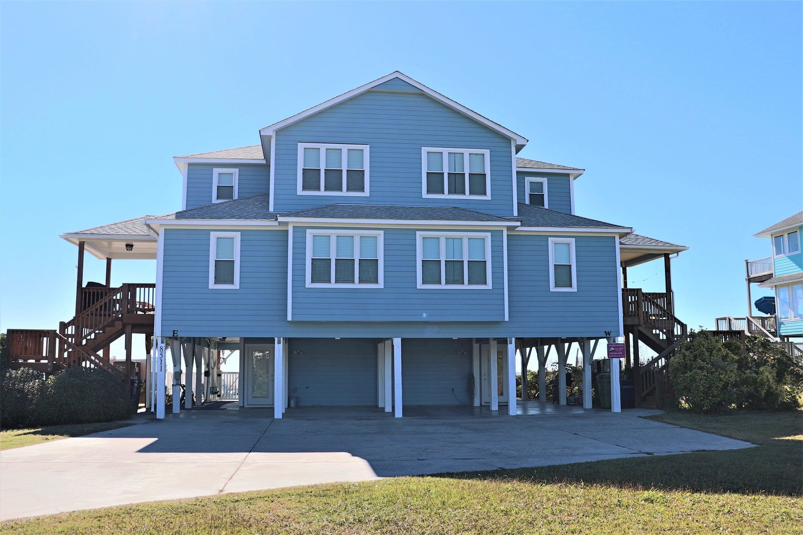 A charming blue coastal home elevated on stilts with covered parking and wooden stairs leading to wraparound porches.