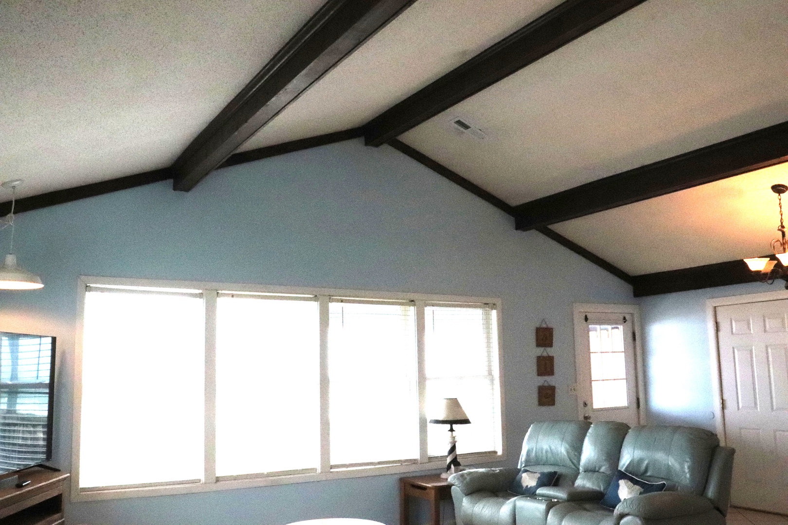 Step into your cozy retreat with vaulted ceilings and warm wooden beams creating an inviting atmosphere. Relax on the plush recliner as natural light fills your bright living space.
