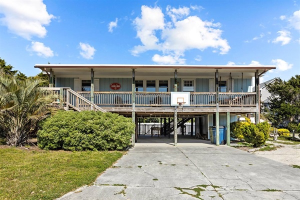 Elevated beach house with spacious covered parking and lush tropical landscaping under sunny Florida skies.
