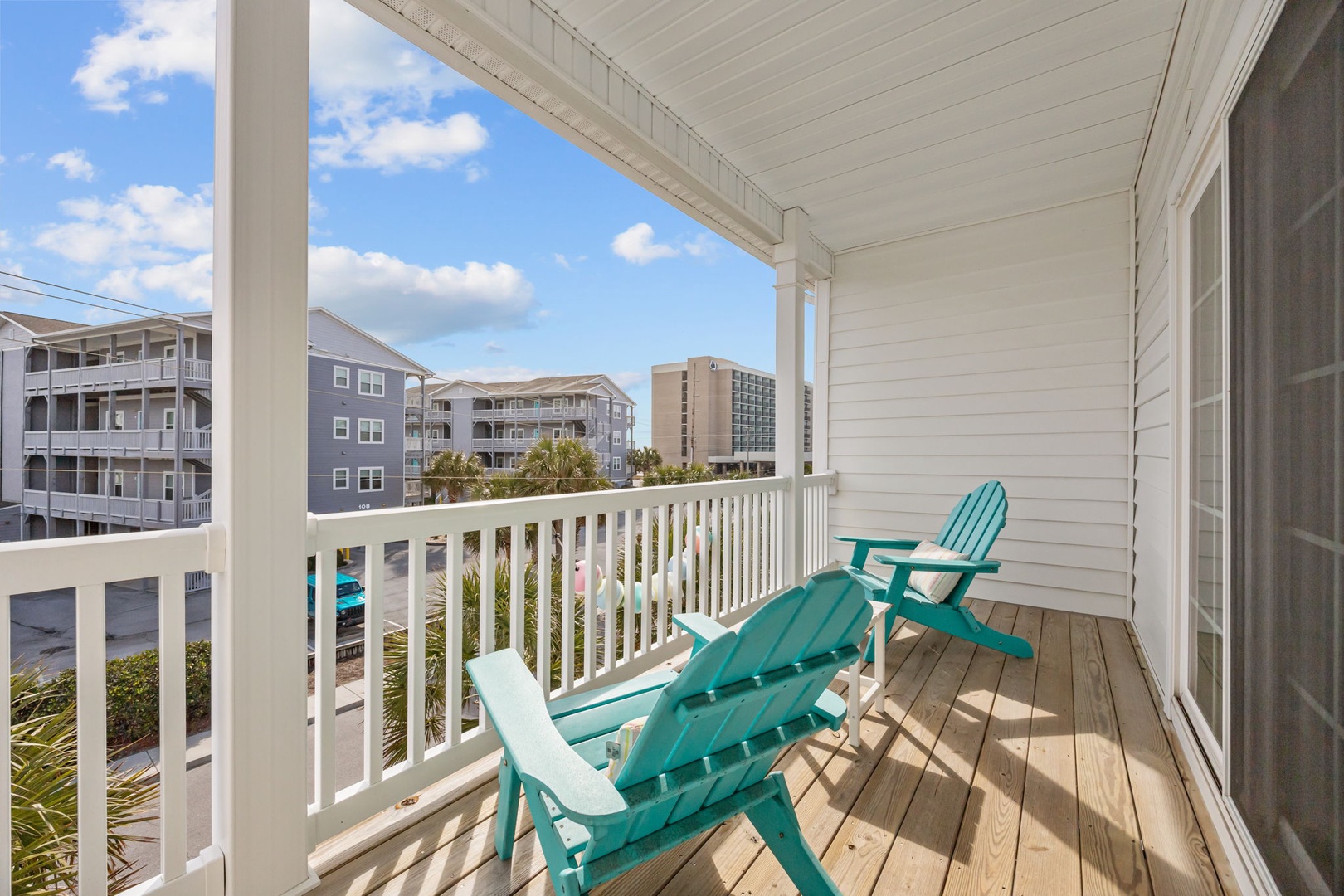 Relax in your private balcony haven with turquoise Adirondack chairs and coastal views stretching beyond palm trees.