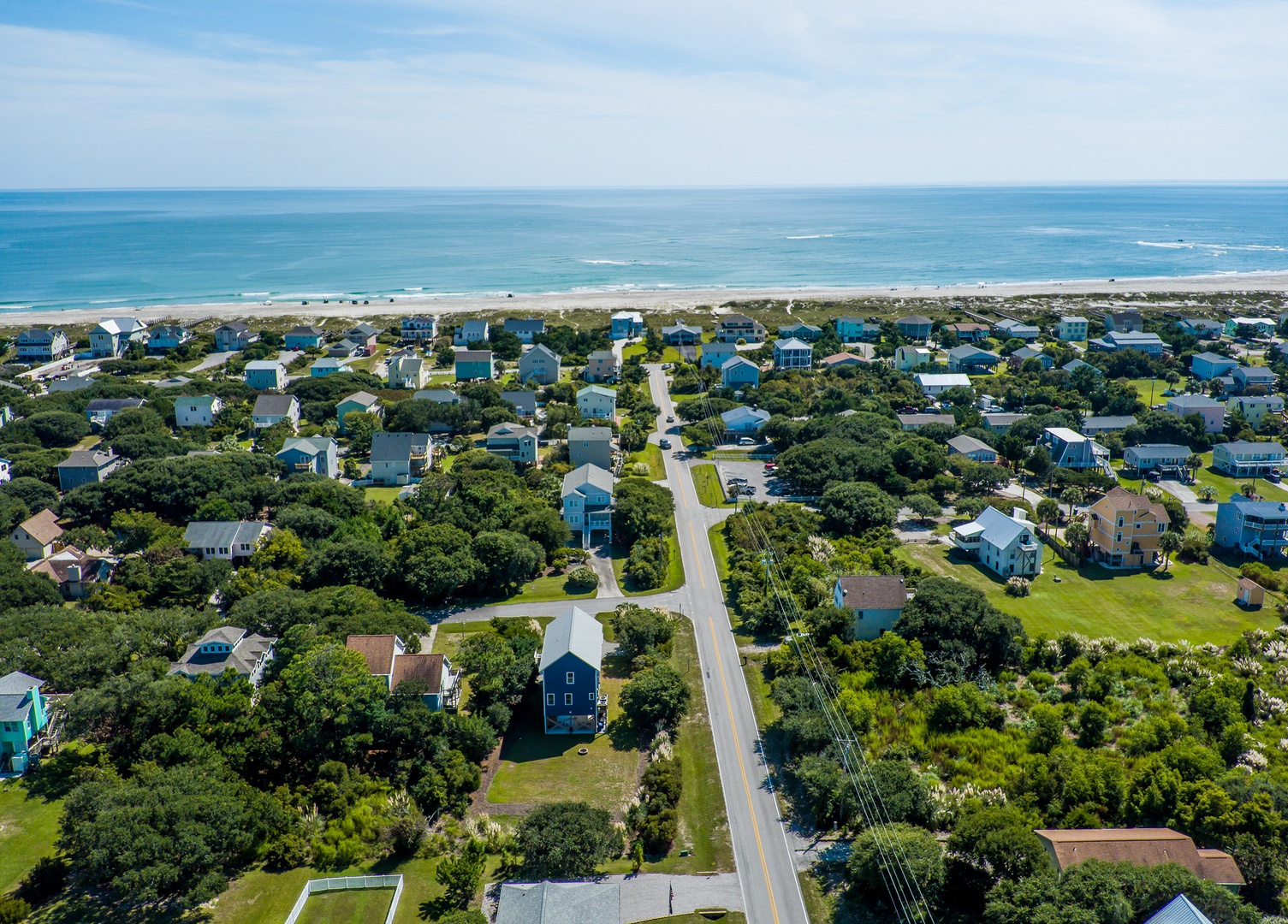 Aerial view of a charming coastal neighborhood with tree-lined streets leading to pristine beaches and ocean waters.