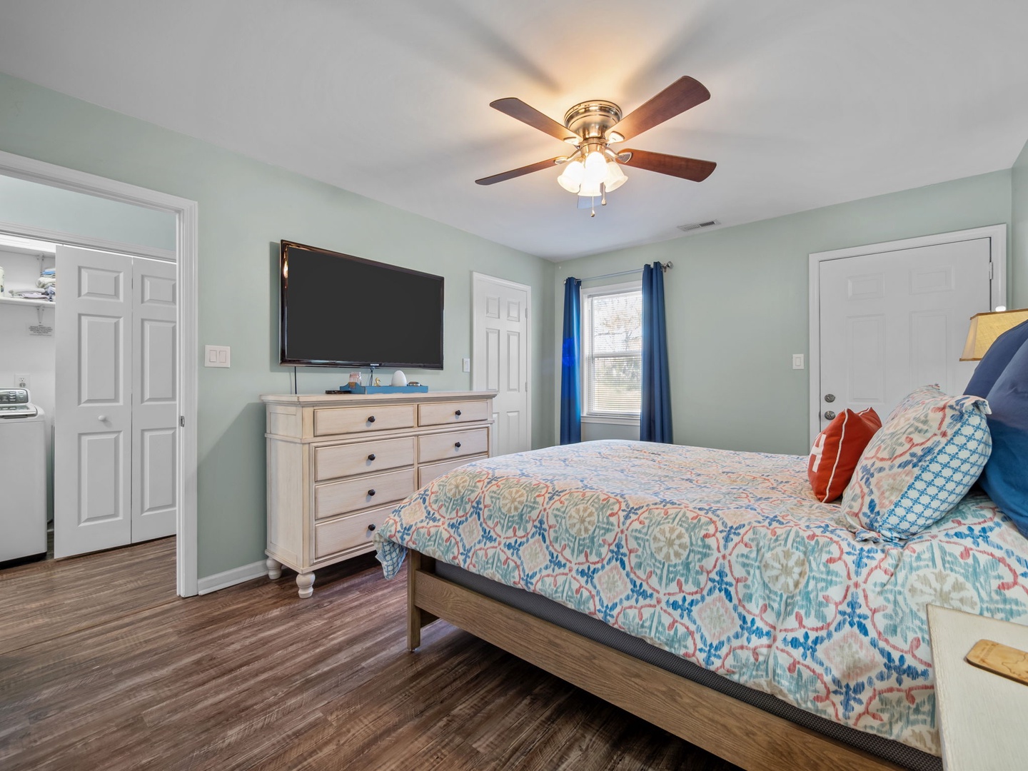 Relax in your peaceful bedroom with coastal-inspired decor, featuring a ceiling fan to keep you cool and a wall-mounted TV for evening entertainment.