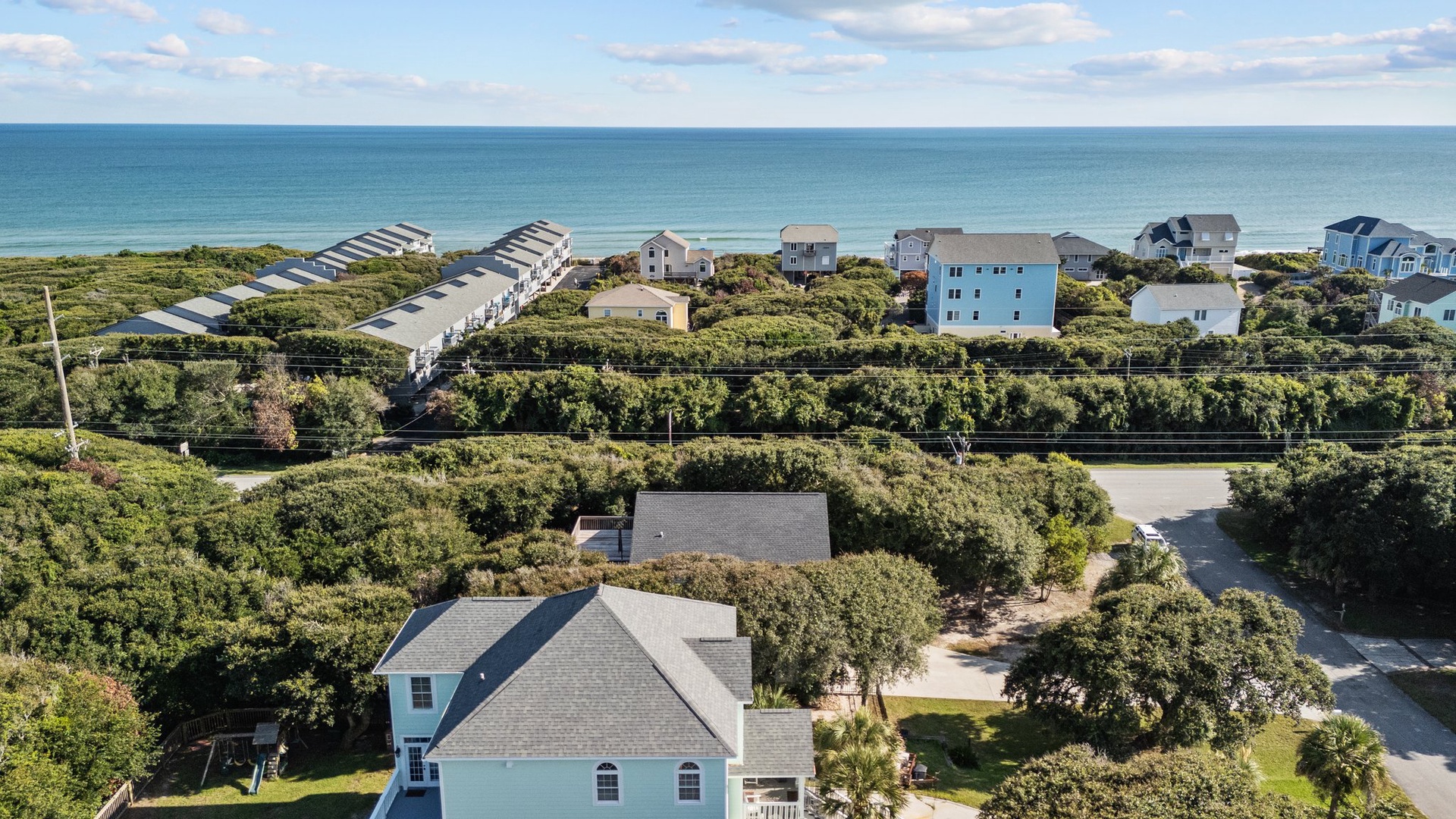 Aerial view of coastal vacation homes nestled among lush maritime forest, just steps from pristine oceanfront beaches.