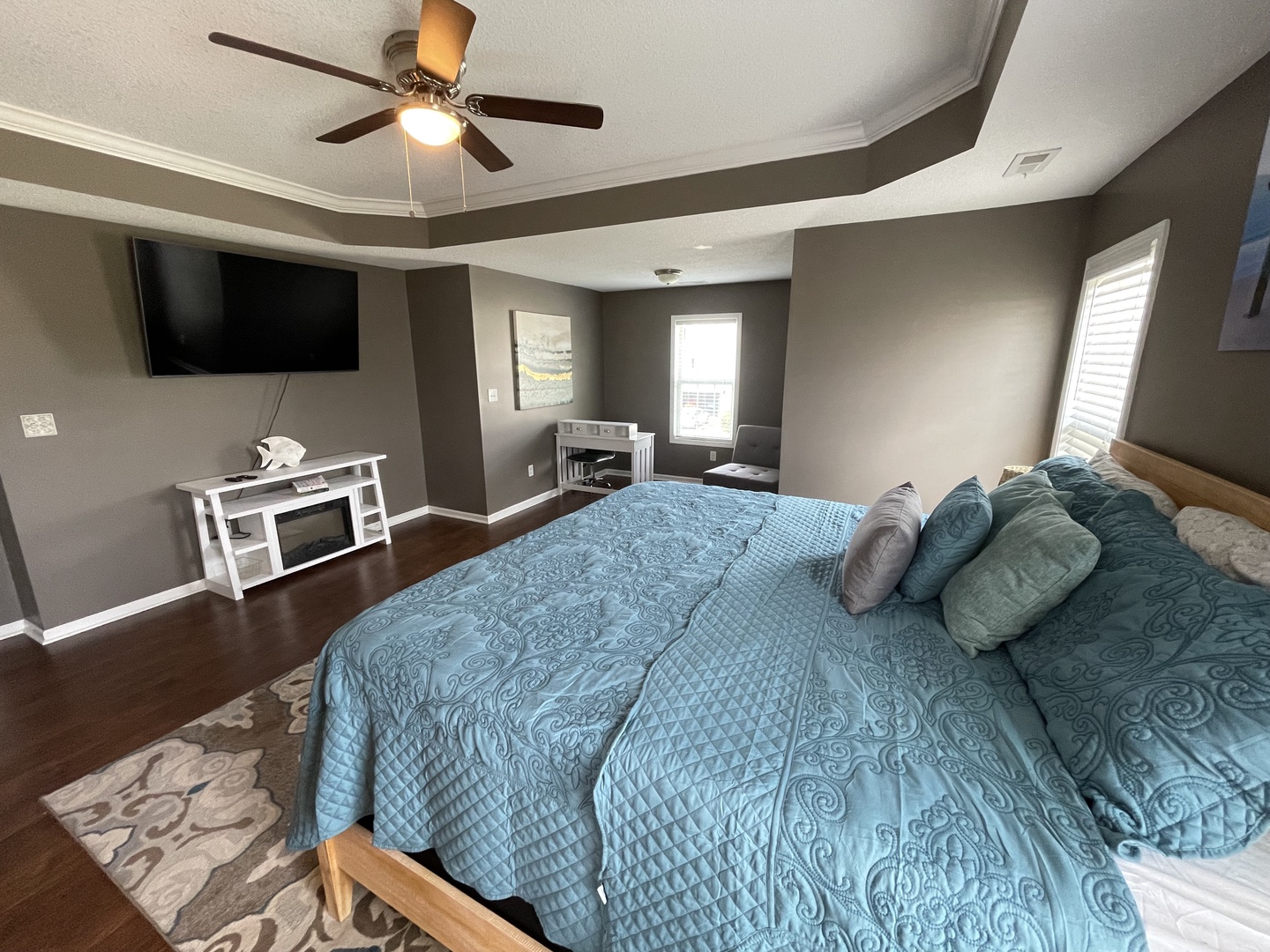 Relax in your spacious bedroom featuring a ceiling fan, cozy fireplace, and entertainment center for ultimate comfort.
