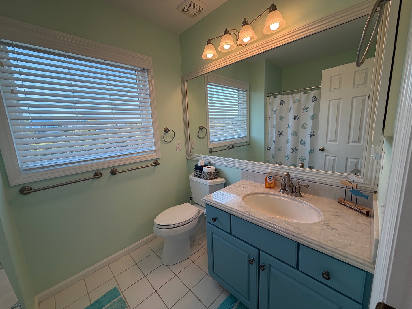Refresh in your tranquil coastal bathroom featuring soft green walls and charming turquoise vanity with marble countertop.