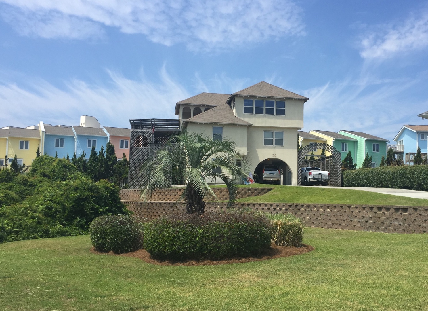 Coastal rental home featuring elevated architecture with ground-level parking and colorful neighboring beach houses creating a charming seaside community.