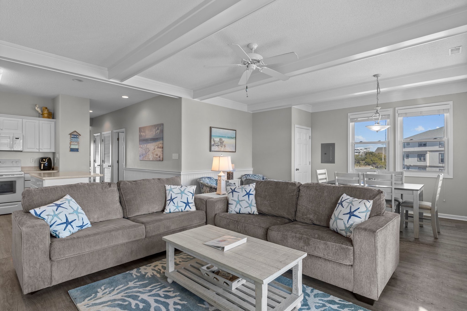Settle into your bright, coastal-inspired living space where soft gray sectionals invite relaxation and coffered ceilings add elegant charm overhead.
