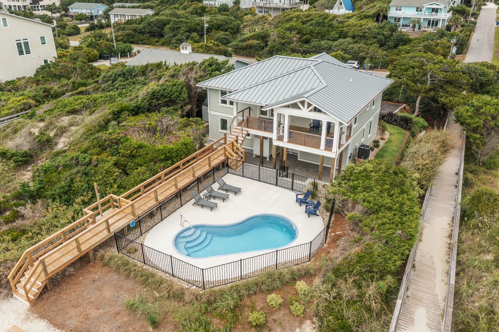 Elevated beach house with private pool nestled among coastal vegetation, featuring wooden walkway access through natural dune landscape.