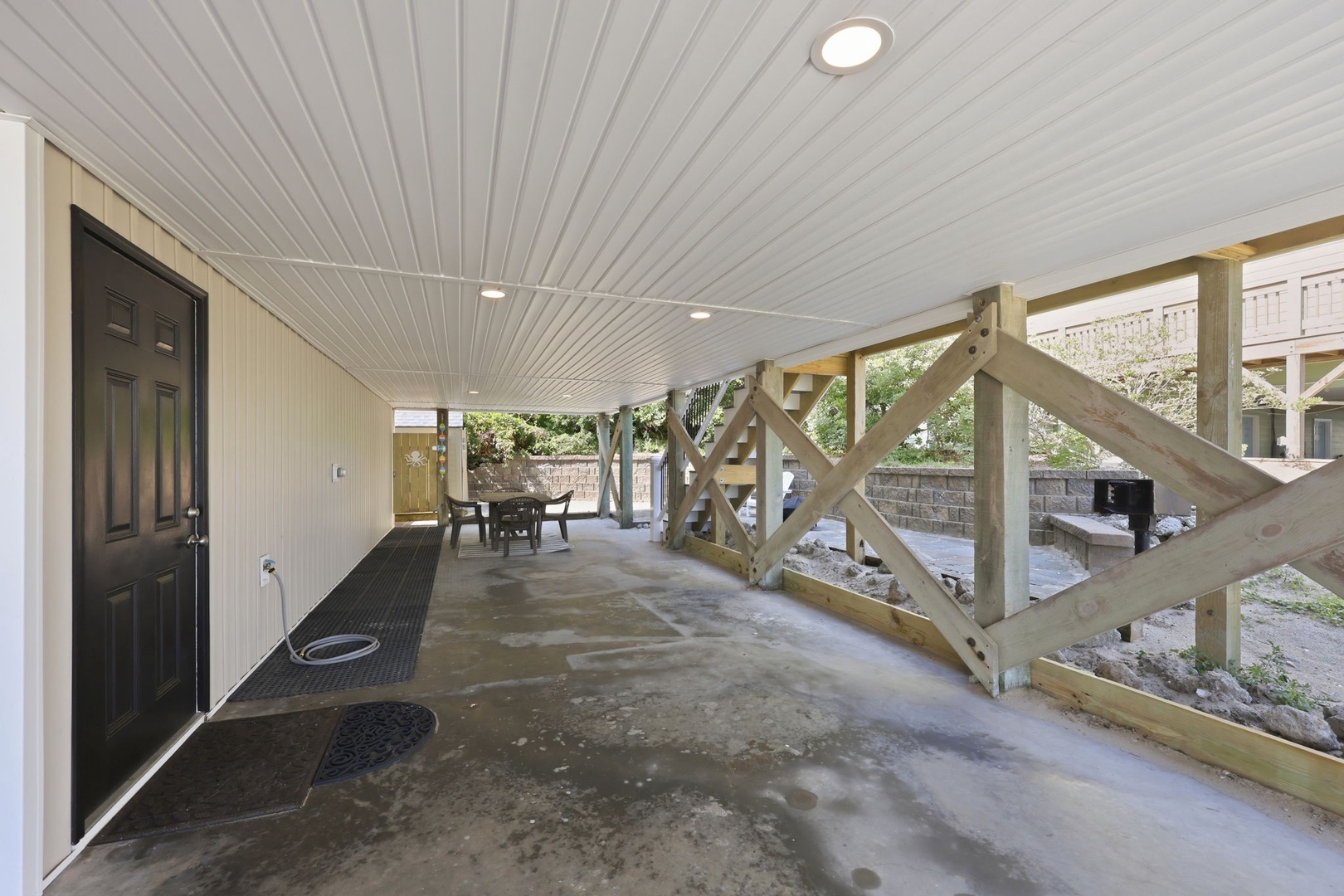 This covered ground-level entry area features a sheltered walkway leading to your private entrance, with an outdoor dining space visible in the background and easy parking access nearby.