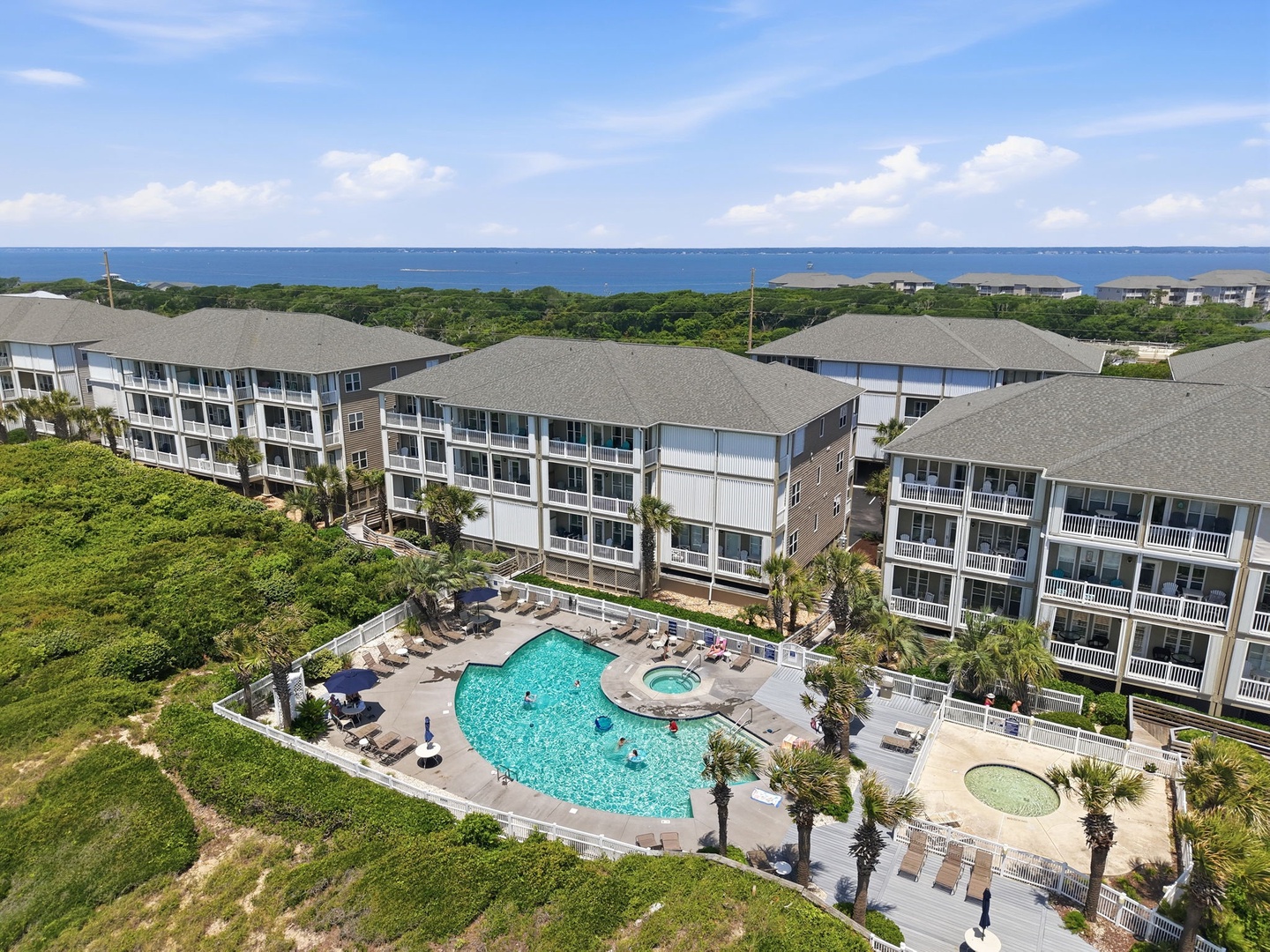Coastal resort property featuring an expansive pool complex and hot tub, surrounded by lush tropical landscaping and just steps from the ocean.